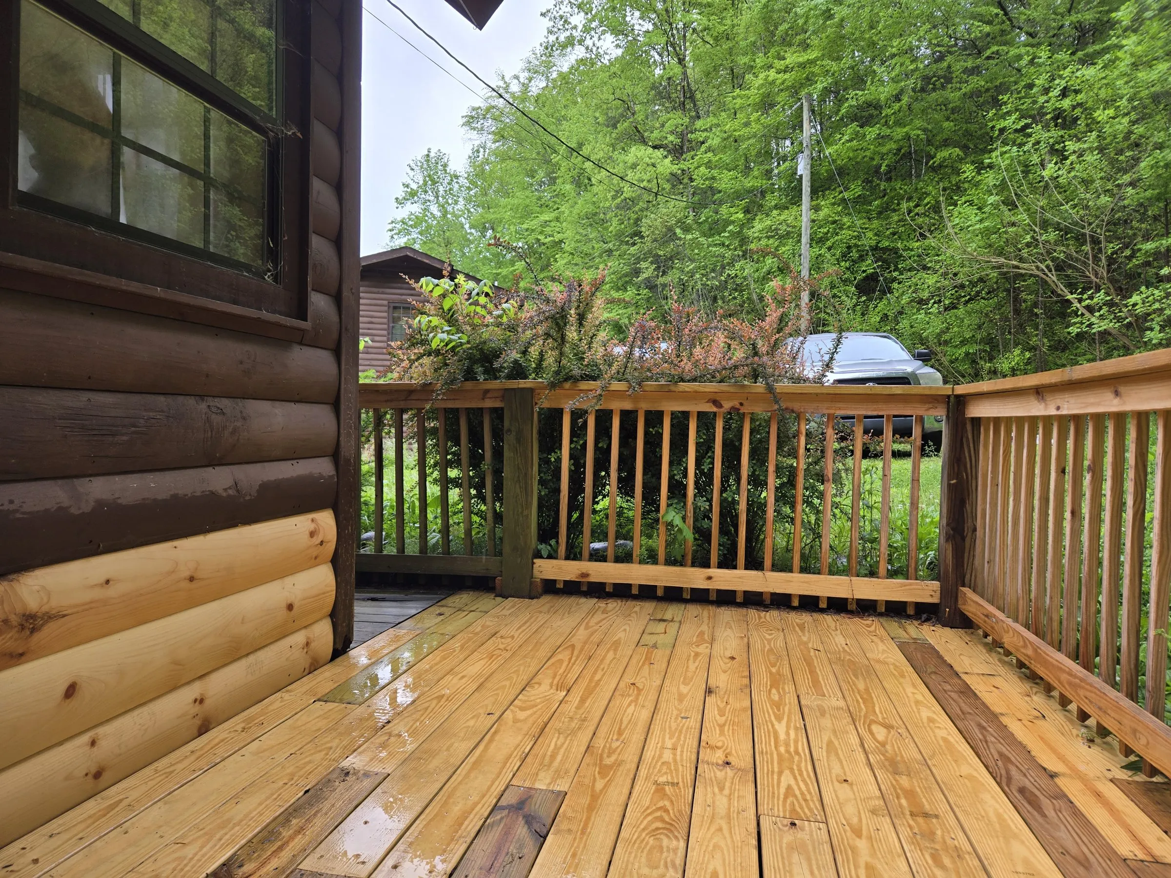 A cabin deck corner in April 2024, with new boards, new railing and new log siding